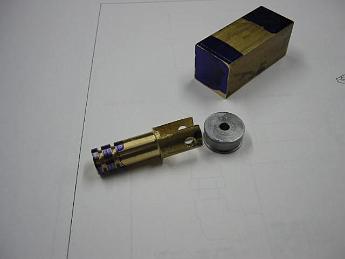 Crab_Parts_Oct_2002 005 I started working on the water pump assembly.  Shown is the pump ram made from brass, and follower roller in steel.  Waiting with layout blue ends is the pump body.  Based on the drawings, I will scribe lines in the layout blue showing where the cuts and holes need to be.  Oct-2002.